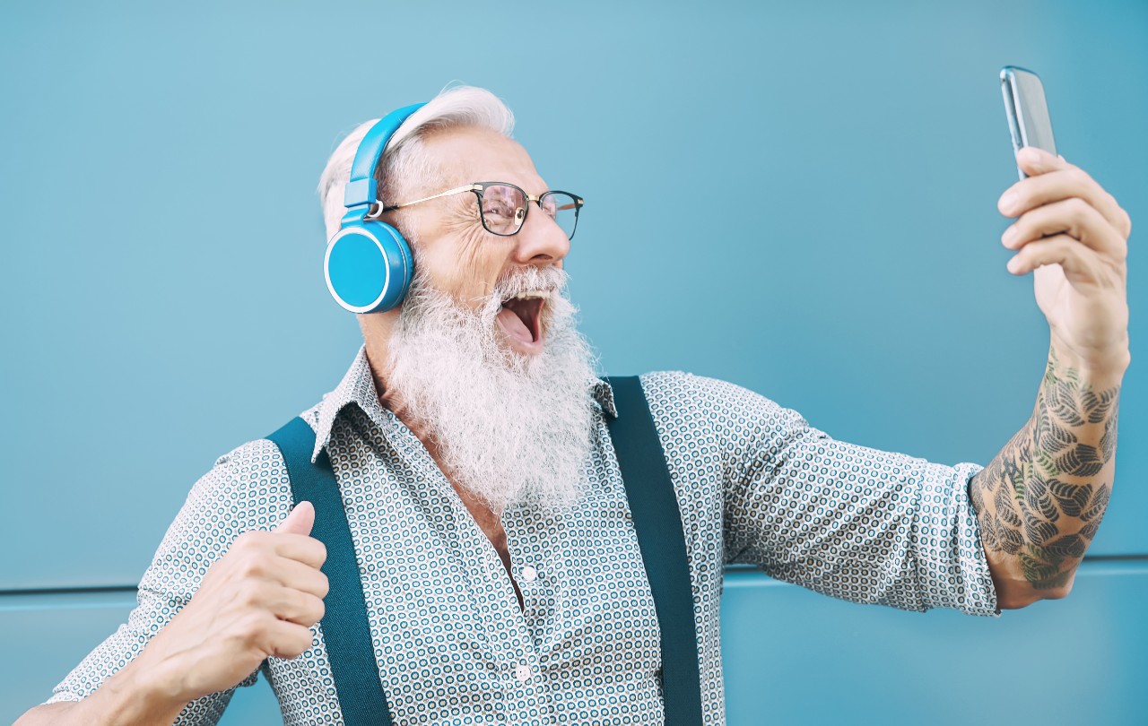 Homme âgé heureux prenant un selfie tout en écoutant de la musique avec des écouteurs.