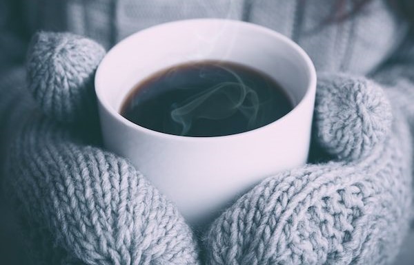 Mains avec gants tiennent une tasse de café chaude
